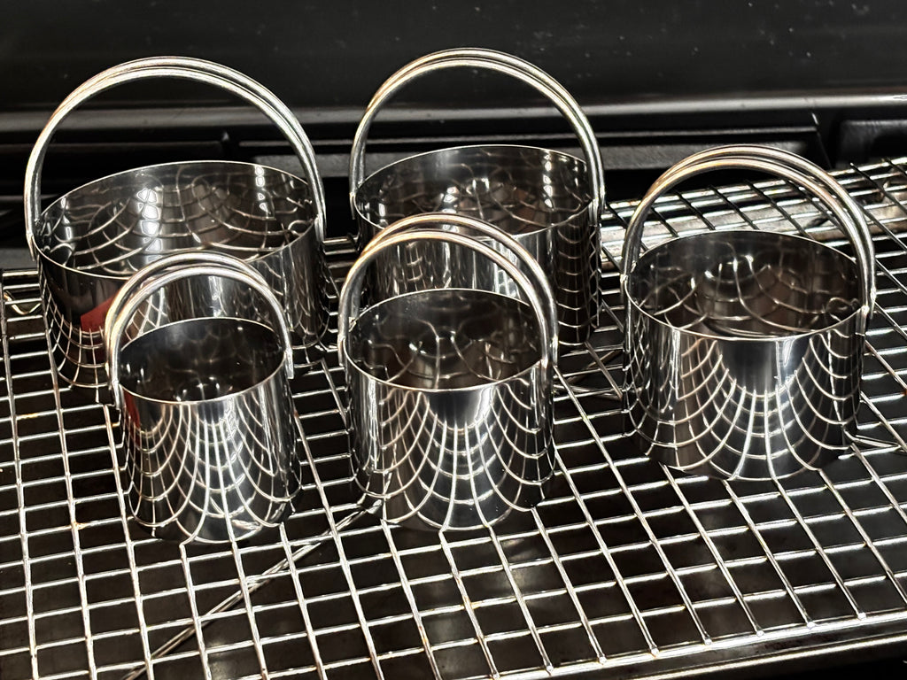 Four stainless steel biscuit cutters with loop handles air-drying on a wire cooling rack, showing their polished interior and sturdy construction — Fox Run