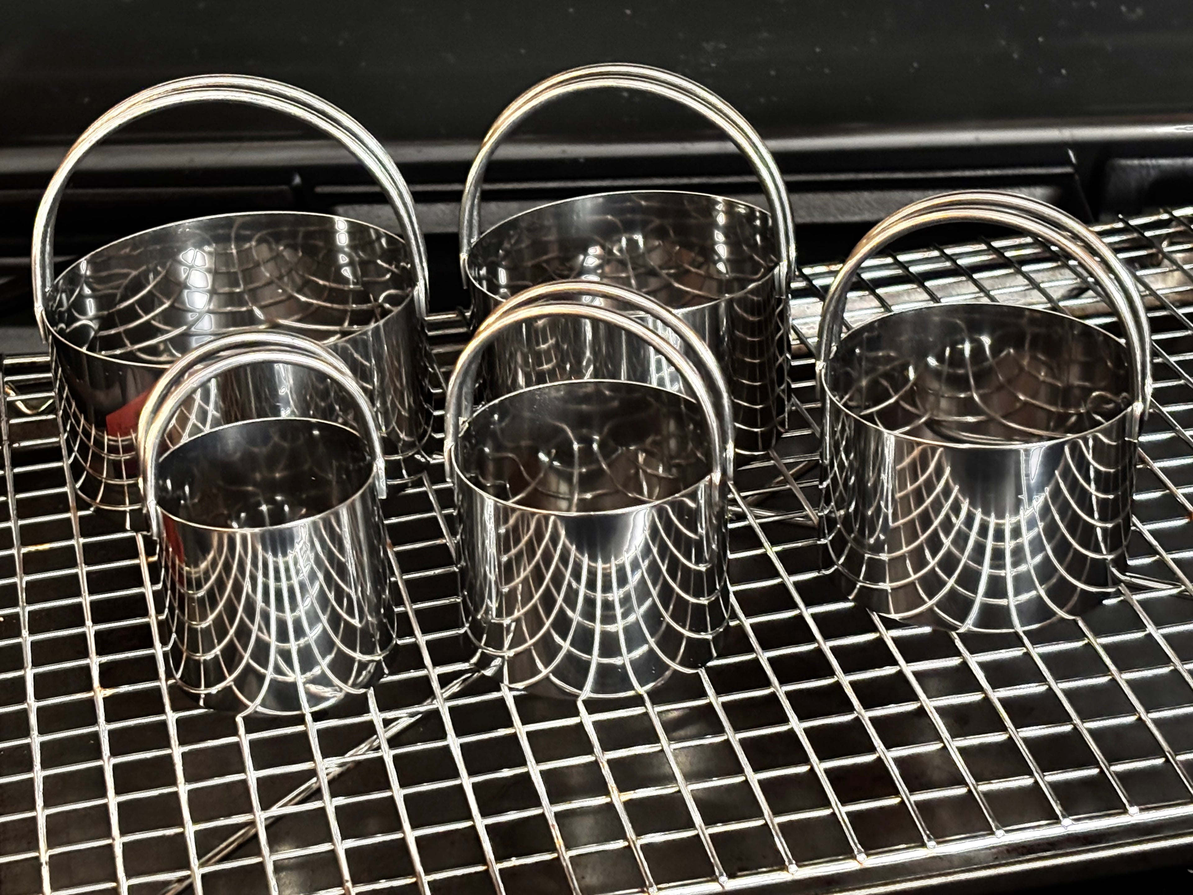 Four stainless steel biscuit cutters with loop handles air-drying on a wire cooling rack, showing their polished interior and sturdy construction — Fox Run