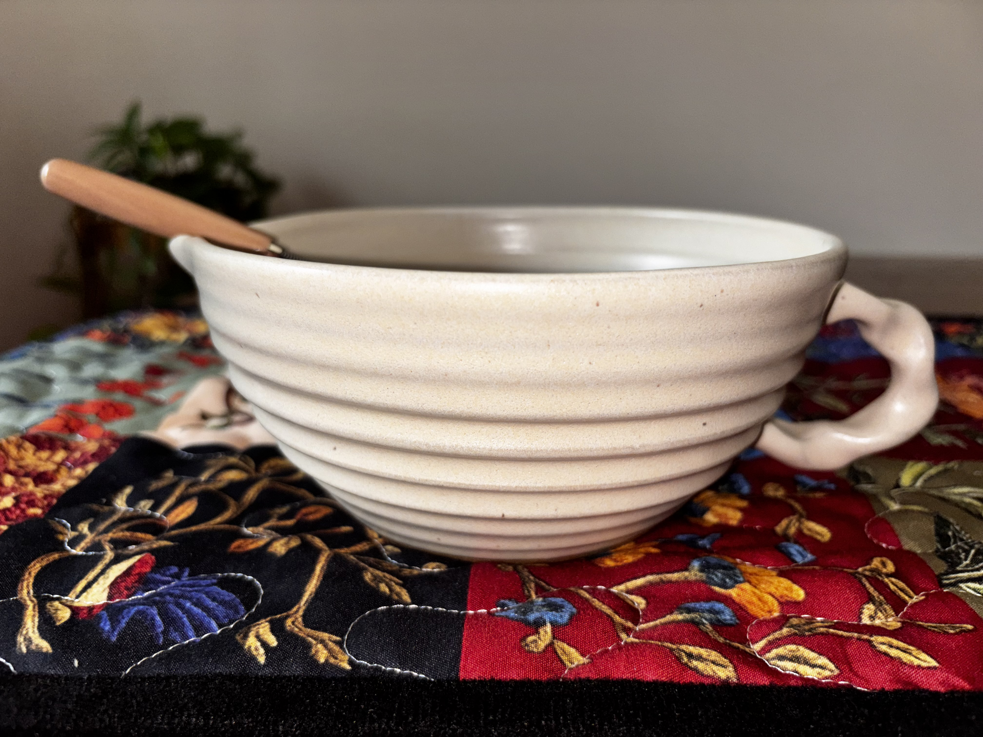  "Single Gravesco handmade cream ceramic mixing bowl on colorful quilted runner with whisk handle resting on left side"