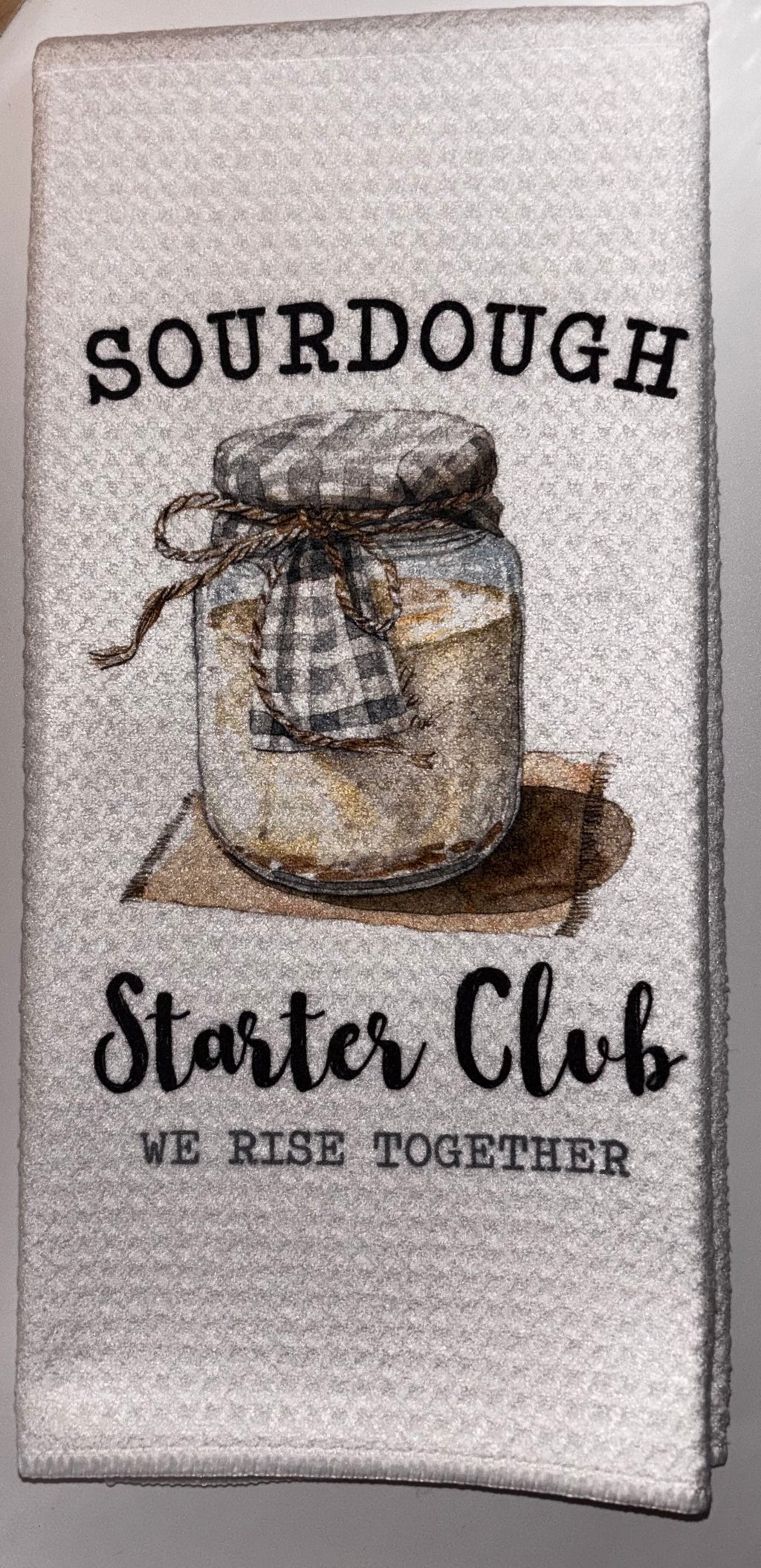 White Sourdough Starter Club kitchen towel with an illustrated starter jar and the words “We rise together.”
