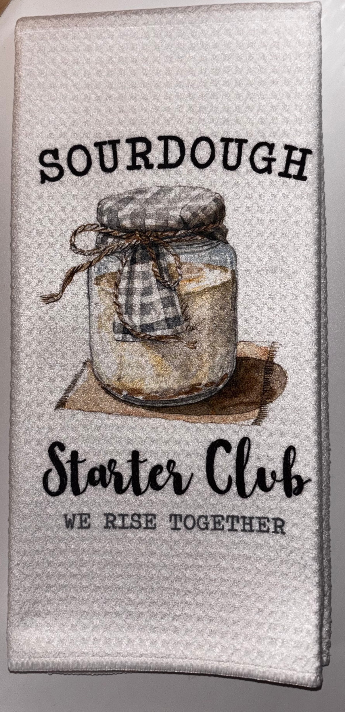 White Sourdough Starter Club kitchen towel with an illustrated starter jar and the words “We rise together.”
