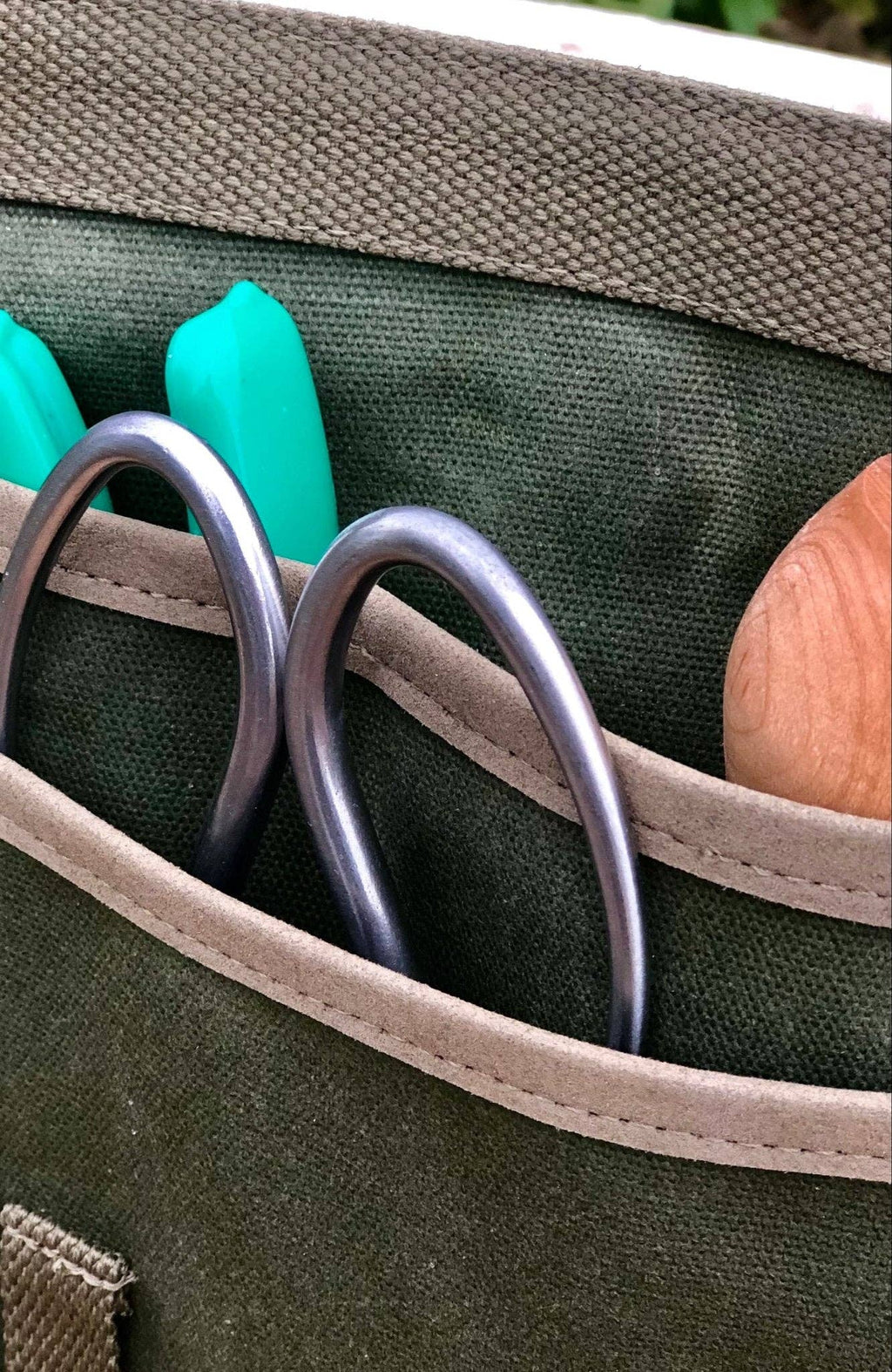 Close-up of the garden tool belt’s canvas pockets holding green-handled and metal gardening tools.