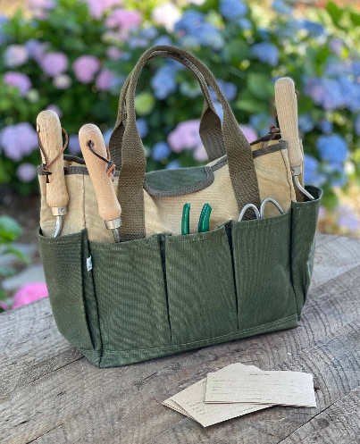 Celtic Farm hunter green waxed canvas garden tote loaded with tools on wooden surface with hydrangeas in background