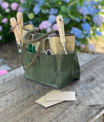 Celtic Farm hunter green garden tote filled with garden tools on wooden table with colorful garden in background