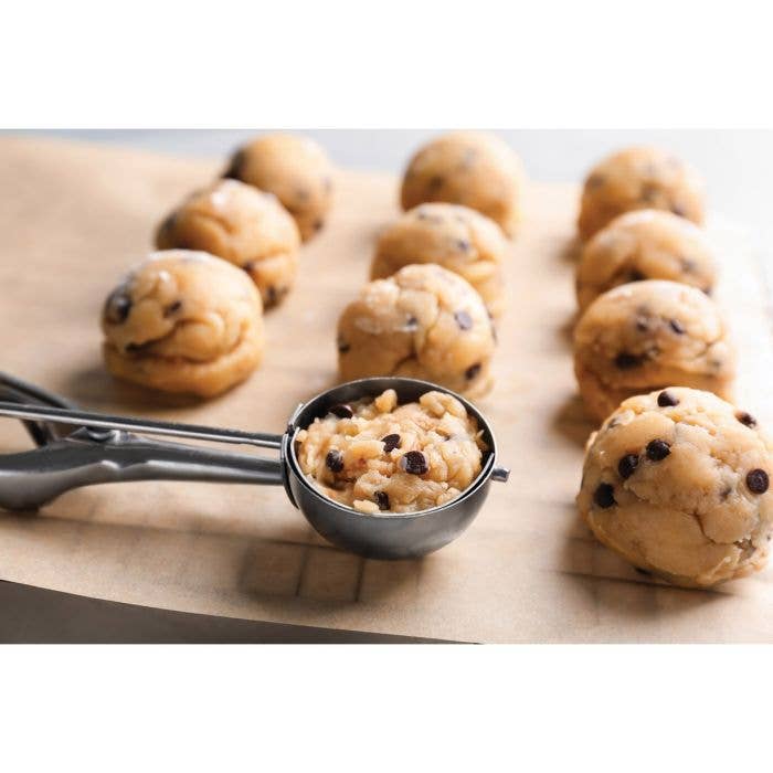 Rows of perfectly portioned chocolate chip cookie dough balls on parchment paper with the Mrs. Anderson's No. 40 cookie scoop in the foreground, showing uniform sizing.
