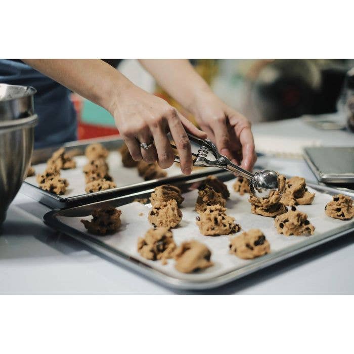 Hands using the Mrs. Anderson's Baking No. 40 cookie scoop to portion uniform rounds of chocolate chip cookie dough onto a parchment-lined baking sheet.