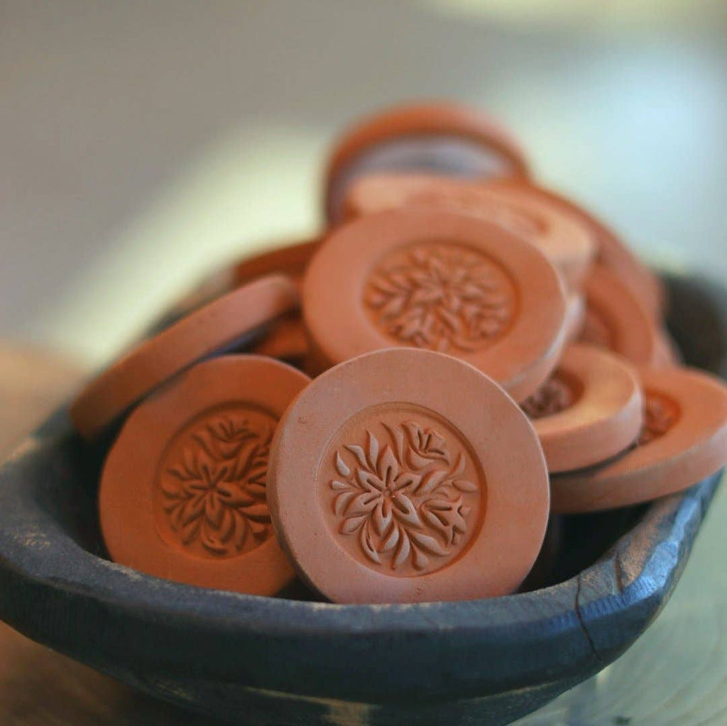 Multiple Gravesco handmade terracotta brown sugar keepers with floral medallion detail displayed in a dark ceramic bowl"
