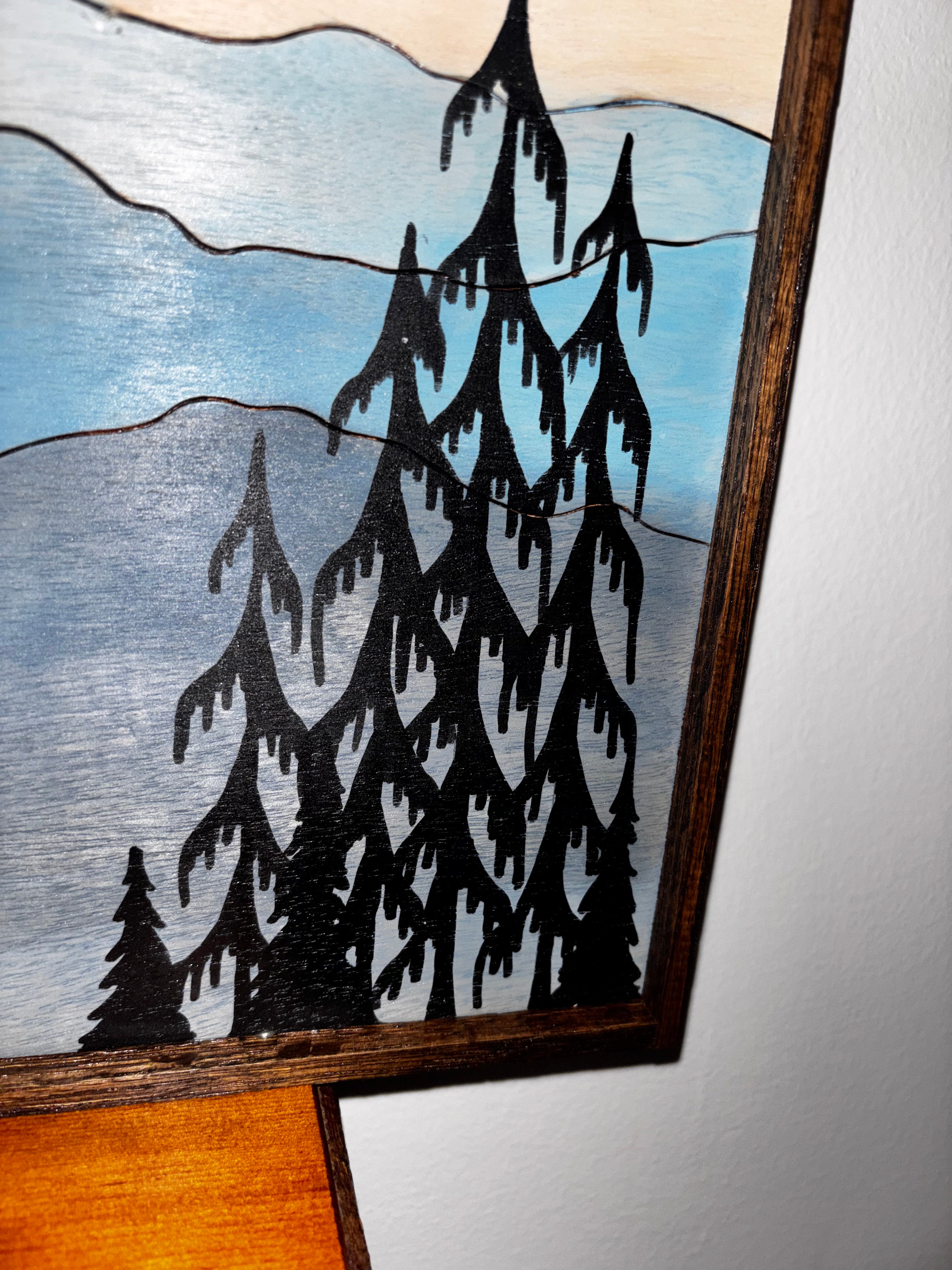Close-up of pyrography pine trees and layered blue mountain peaks on birch plywood wall art
