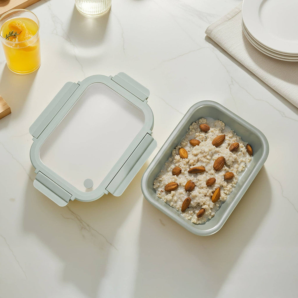 Square storage Container of oatmeal with almonds on a light surface with lid, next to a glass of orange juice.