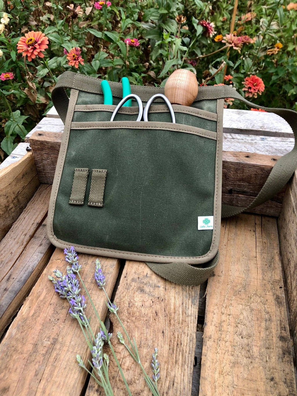 Garden tool belt filled with small tools on a rustic wooden bench beside flowers and lavender.