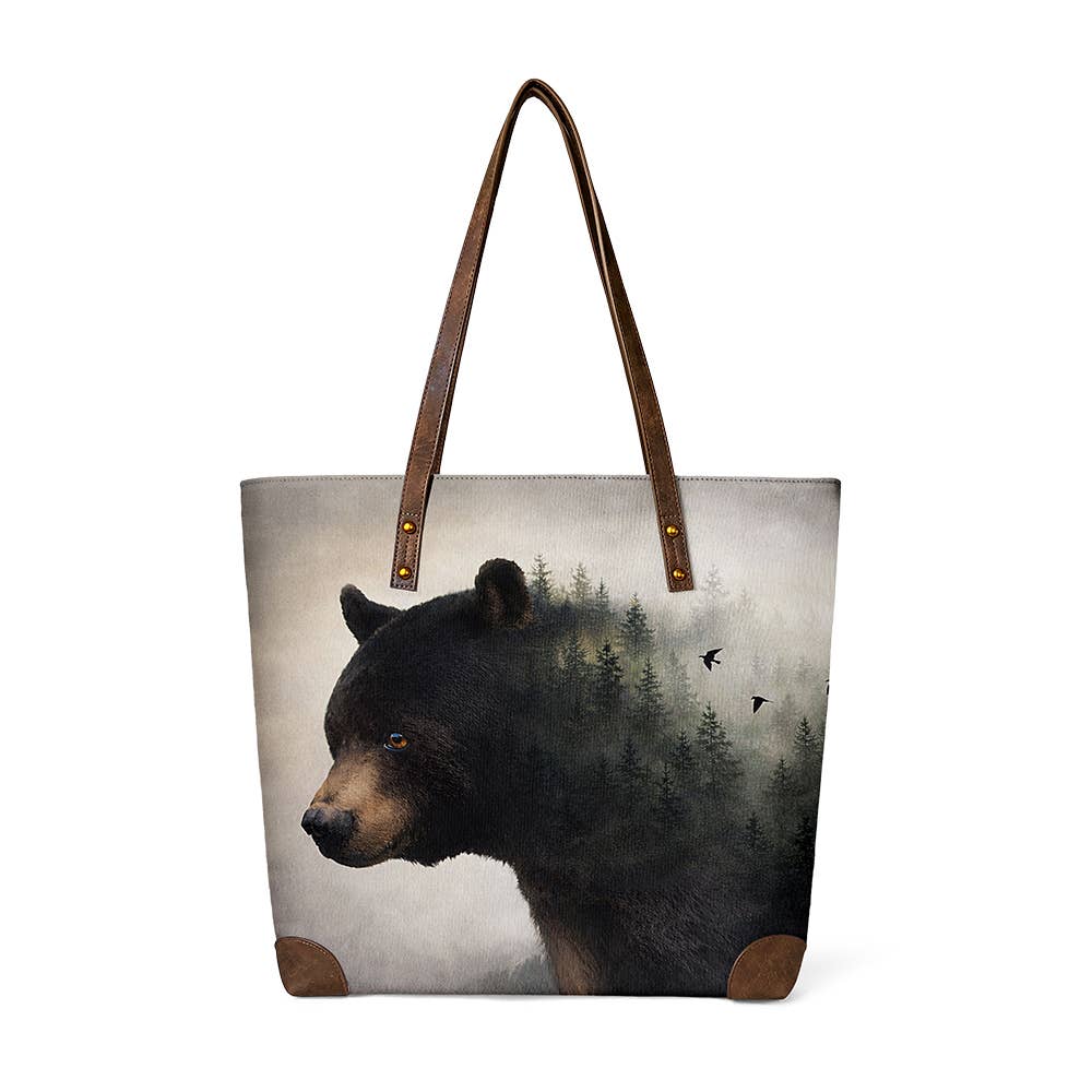 "Forest black bear wildlife art canvas tote bag with misty pine forest and birds in flight design, leather-look shoulder straps, and corner reinforcements on white background