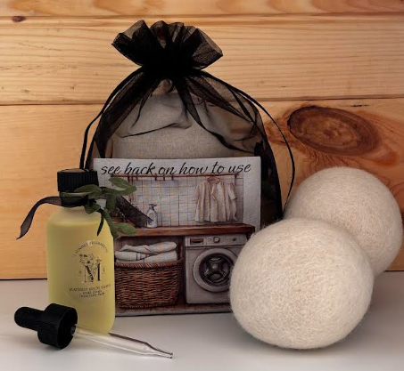 Wool dryer ball gift set showing two white balls beside the scent oil bottle, glass dropper, and instruction card in a black drawstring bag.