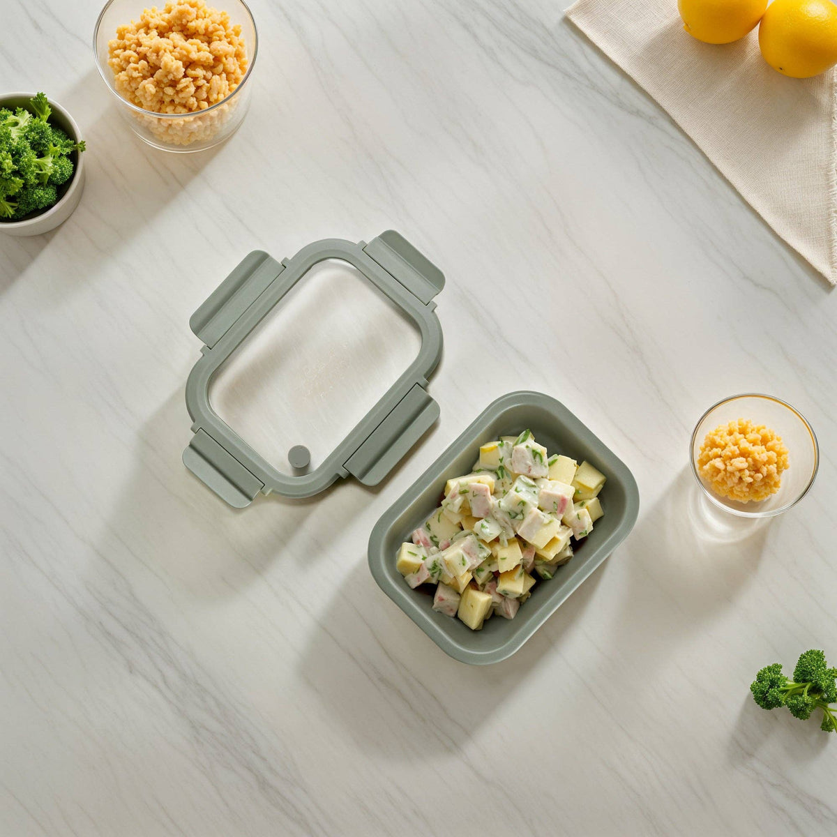 Green food storage container with lid and chicken salad on a light wooden surface