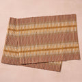 Two placemats fanned/overlapping (blush bg): "Two handloomed 100% cotton placemats in brown, tan, and gold stripe, handcrafted in Nepal by Ten Thousand Villages, shown overlapping on a blush background"