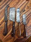 All 4 knives laid out on walnut board, overhead → "Set of four Farmhouse Pottery artisan forged charcuterie cheese knives with hammered steel blades and dark walnut handles with brass rivets, laid out on a walnut wood board overhead view"