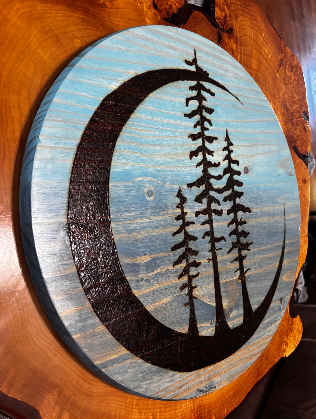 "Side angle view of Tres Luna crescent moon and pine tree wood burn wall art on blue-stained pine round — Adirondack Art Co. by Darren Segool"