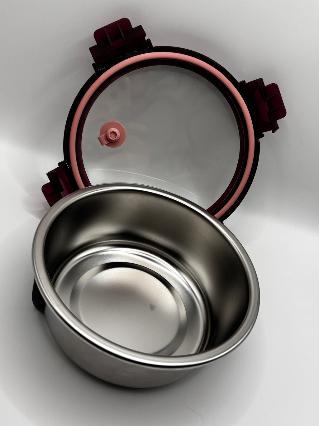 Empty stainless steel food container with the lid removed, showing the pink sealing ring and valve underneath.