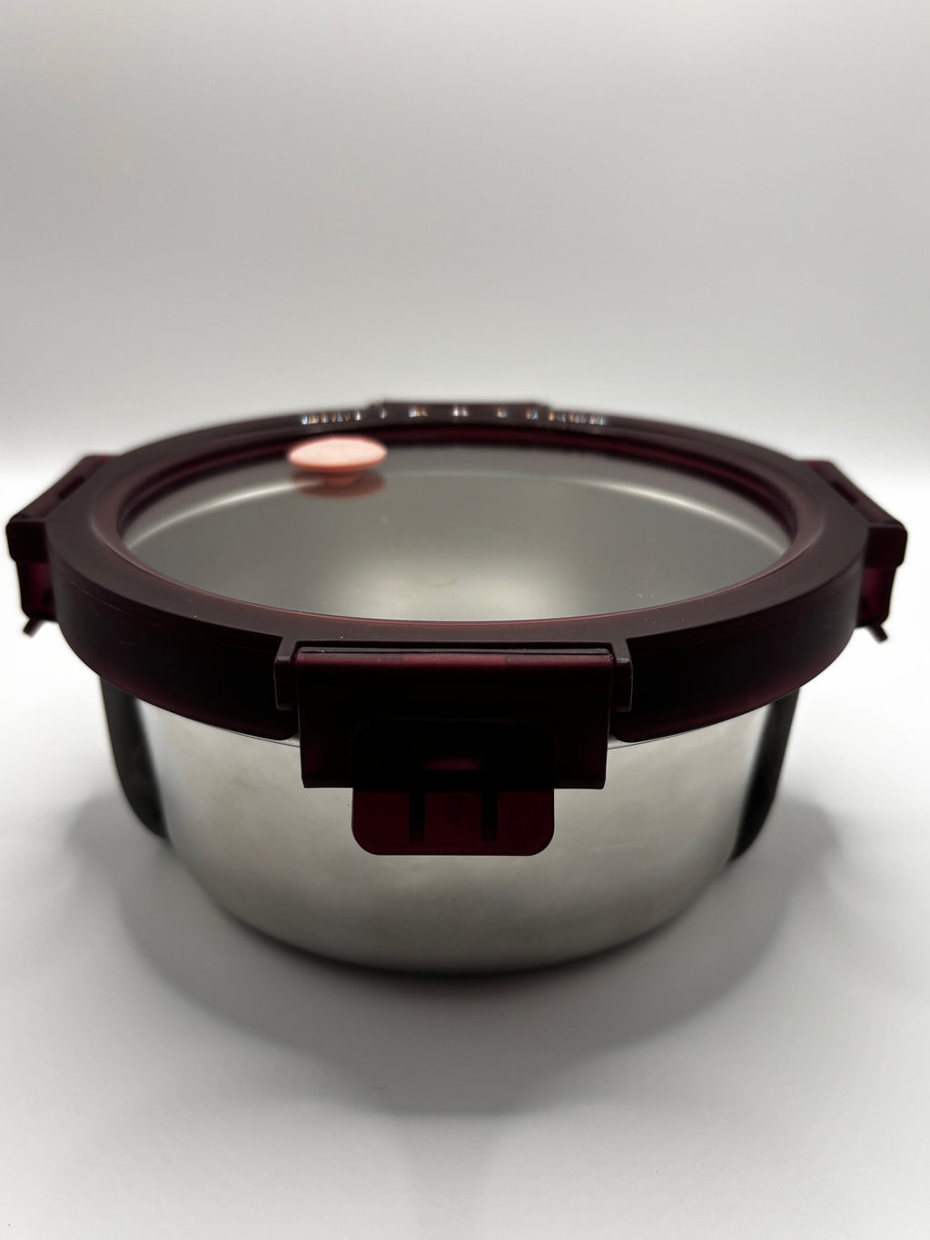 Front view of the stainless-steel container showing its glass lid, burgundy rim, and closed locking clip.