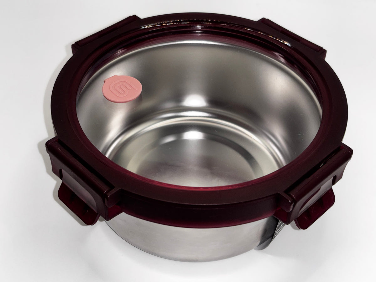 Round Genicook stainless steel food container with a clear glass lid, burgundy locking clips, and a pink valve.