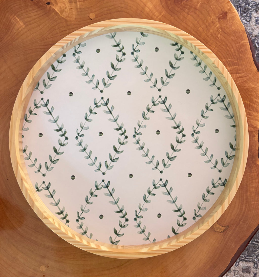 Round wooden tray with a white center featuring green leaf pattern on a wooden surface