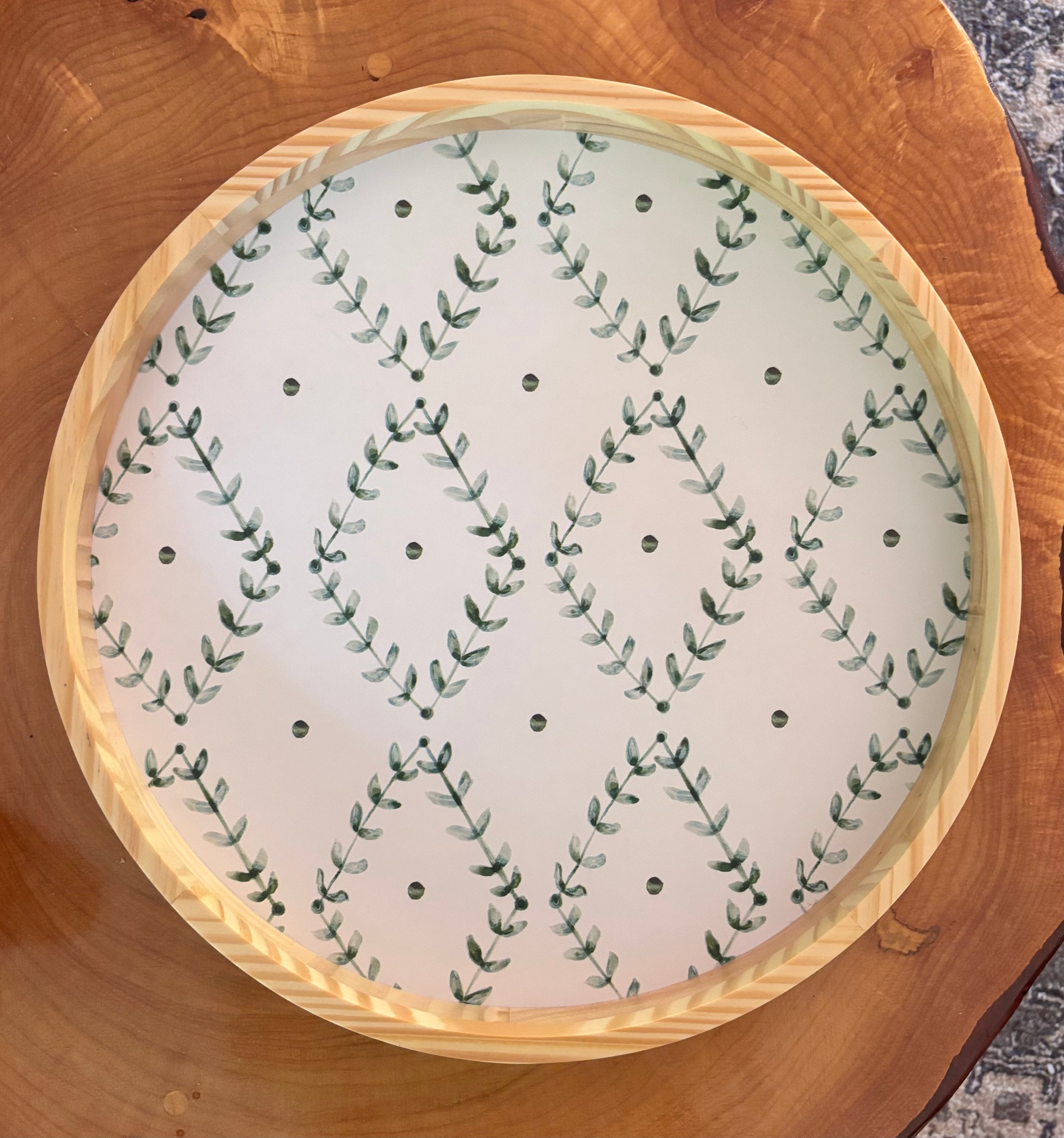 Round wooden tray with a white center featuring green leaf pattern on a wooden surface