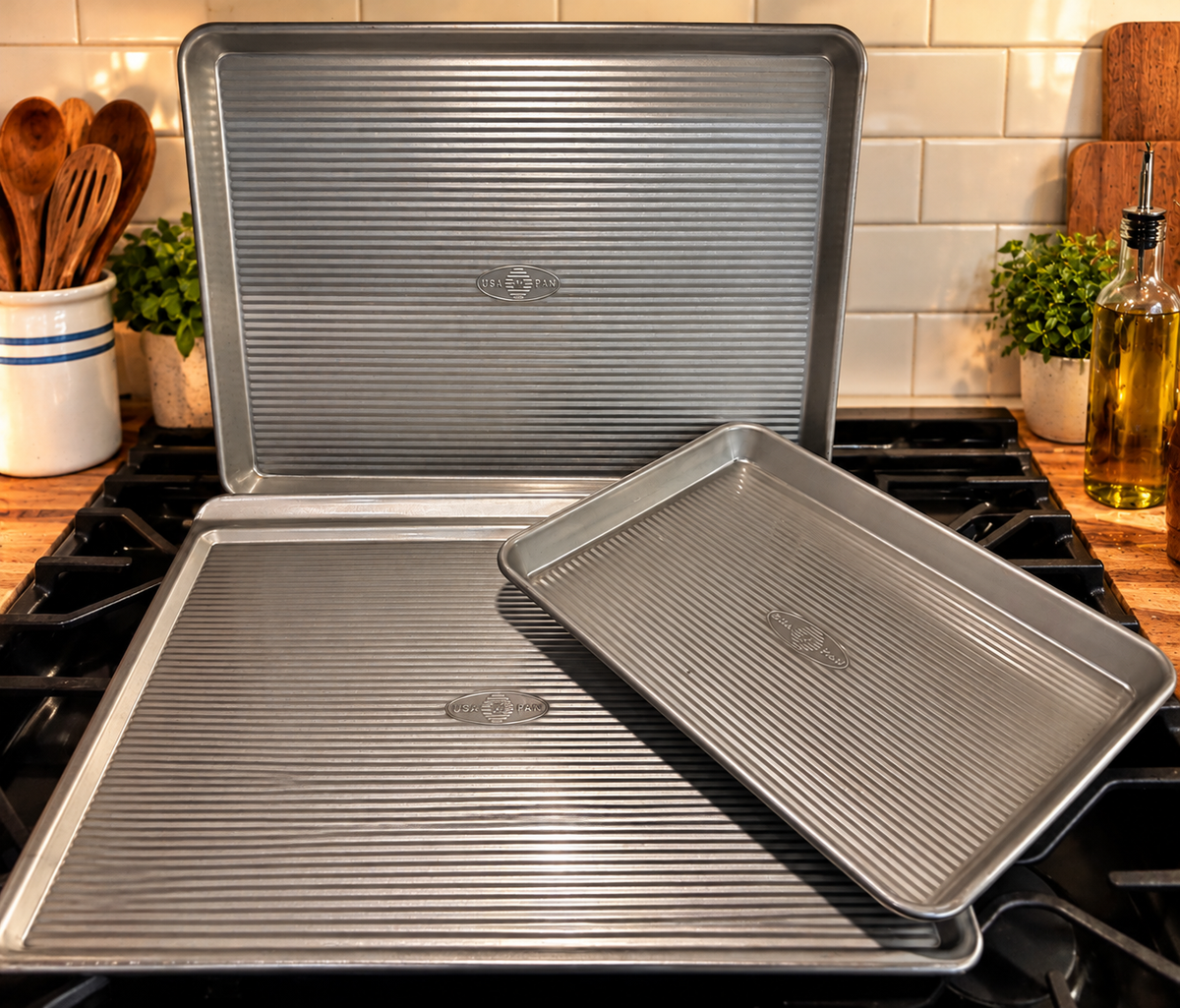 Three USA Pan styles displayed together: a large cookie sheet and two rimmed sheet pans with corrugated surfaces, sold individually.