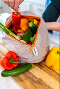 Reusable produce bag with vegetables on a wooden cutting board