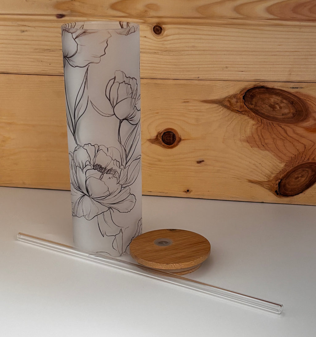 Floral glass tumbler with bamboo lid removed and clear glass straw laid alongside, showing all three included pieces.