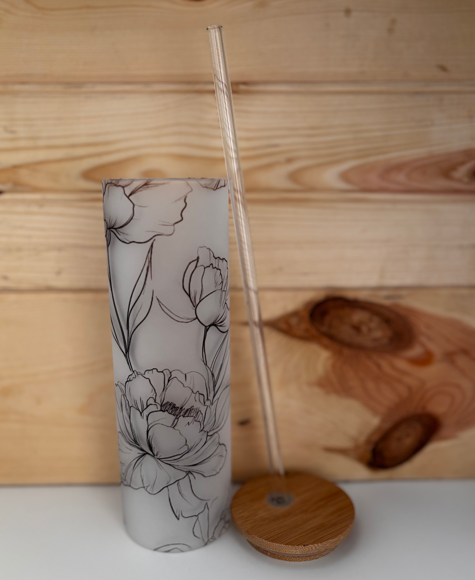 Open frosted floral tumbler beside its bamboo lid, with the clear glass straw standing alongside.