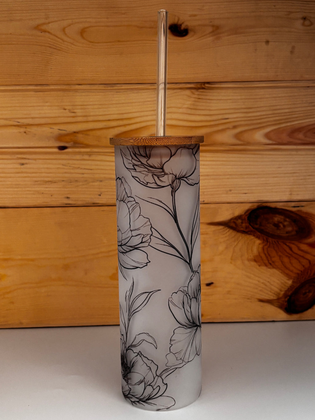 Alternate view of the frosted glass tumbler showing its wraparound peony design, bamboo lid, and glass straw.