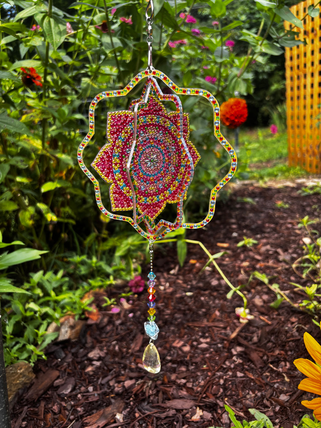  Handcrafted mandala crystal sun catcher hanging in a zinnia garden in full bloom, featuring a hand-placed crystal mandala design with rainbow bead chain and teardrop prism — by Sleeping Whiskers Studio